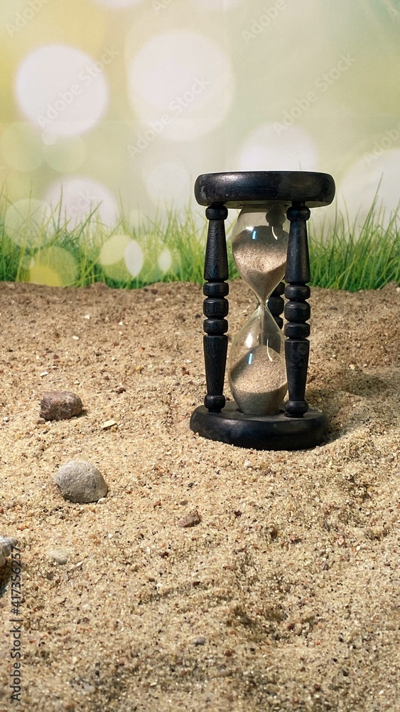 an hourglass measuring the time standing on the sand  - obrazy, fototapety, plakaty 