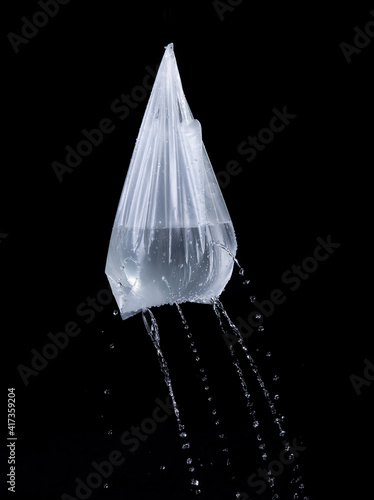 Plastic bag with the water is leaking out the holes on black background
