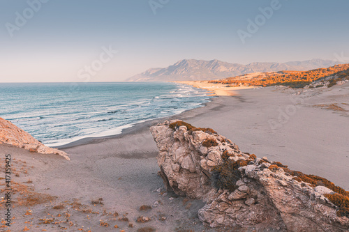 Fototapeta Naklejka Na Ścianę i Meble -  Morning view of the Mediterranean seacoast at the Patara beach during high tide with waves. High mesmerizing rocky cliff in the foreground. Natural wonders of Turkey