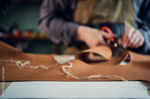 In a boot shop, an experienced young master cuts out leather shoe elements with scissors.