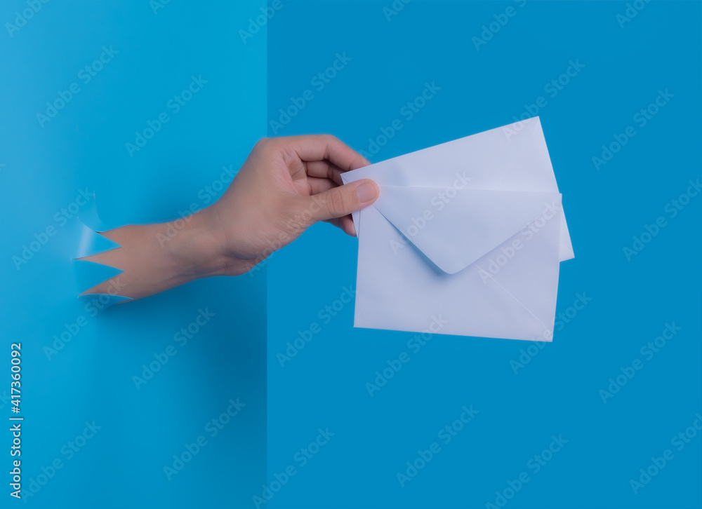 Man's hand holding envelope through the torn blue plastic background