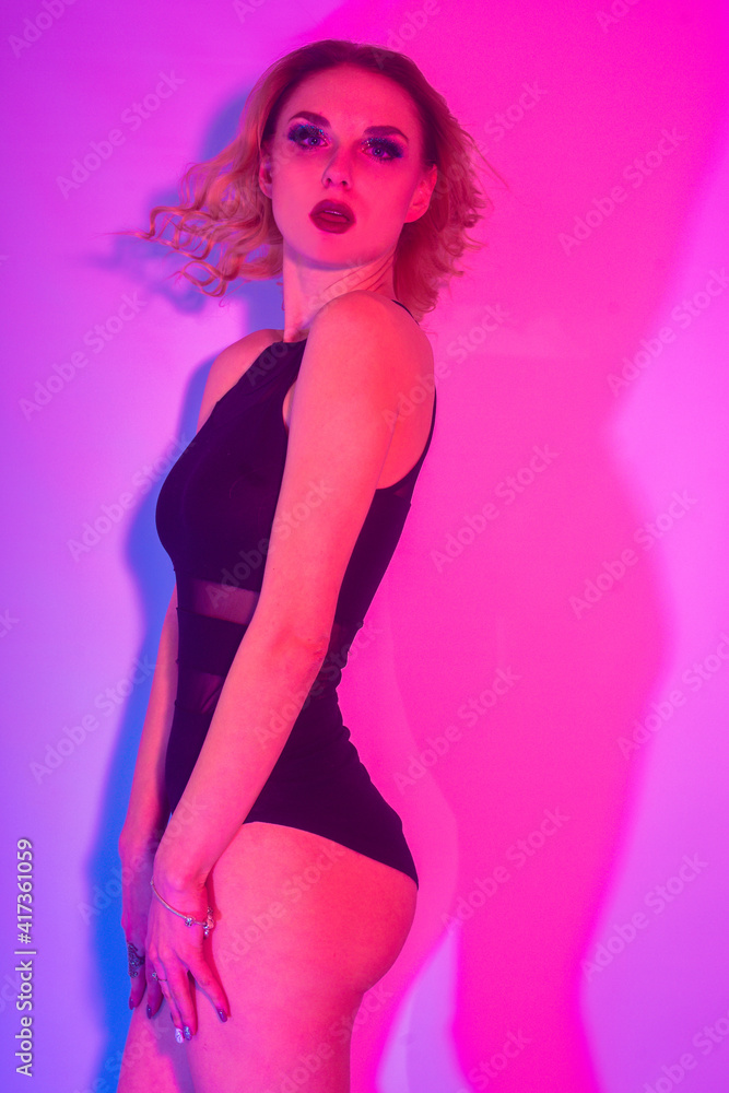 Fashion photo of young  girl on Colored background, studio shot. Beautiful blond woman with red lips curly hair. Woman in neon light. The girl in body dancing go-go, night club. Sexy swimsuit