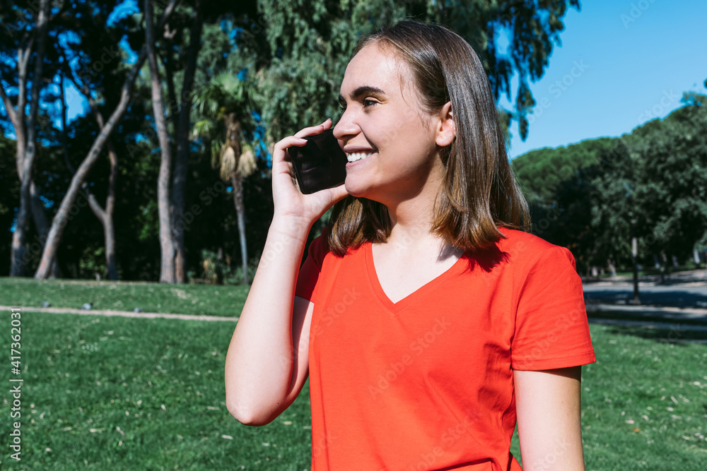 Young blonde woman in a red shirt talks on the mobile phone in a park