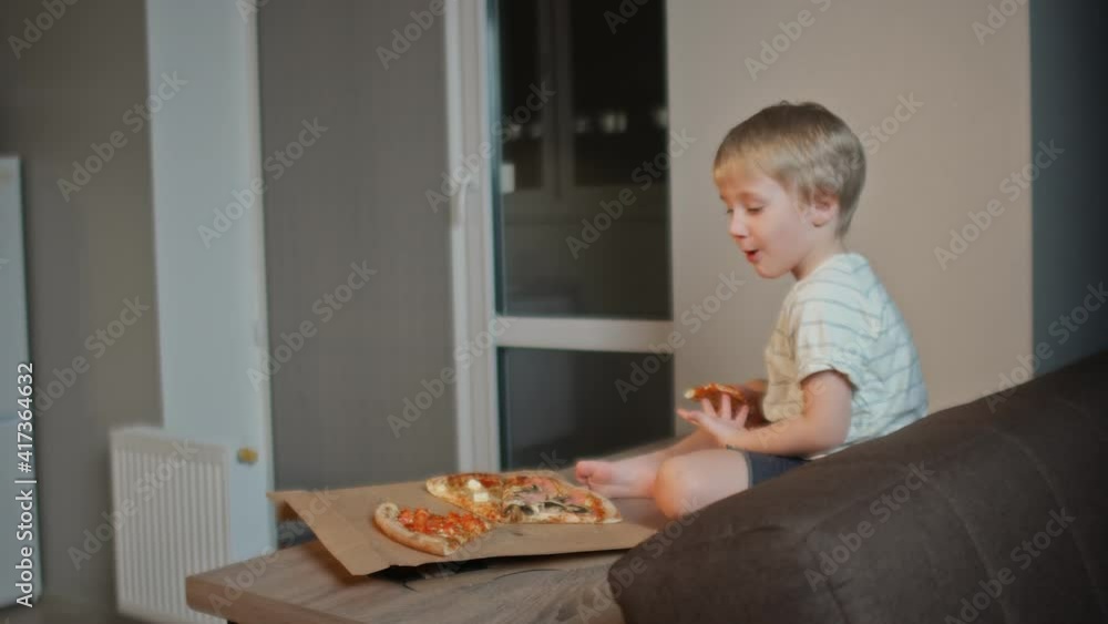 Back view of young little boy sits on table and eats pizza Back view of young little boy sits on table and eats pizza
