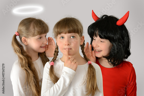 Kid (child) give advice angel and demon whisper in the ear from both sides harmful, useful, evil, good advice concept photography