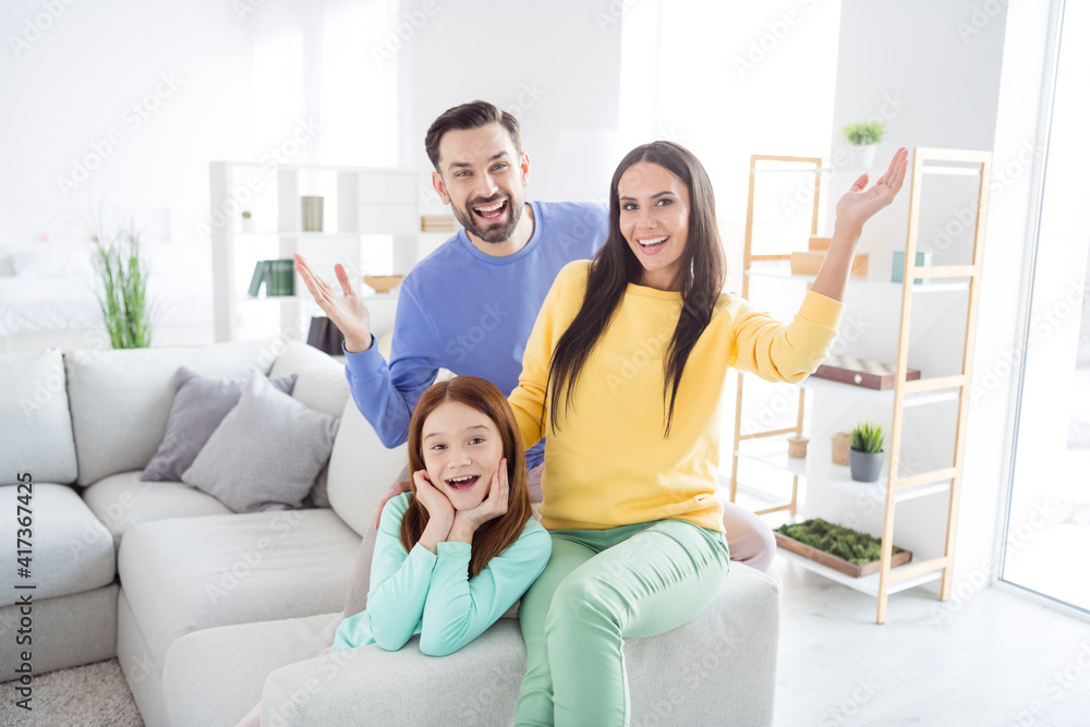 Obraz premium Photo of cheerful family mom dad kid happy positive smile have fun wave hand hello hi sit sofa home together