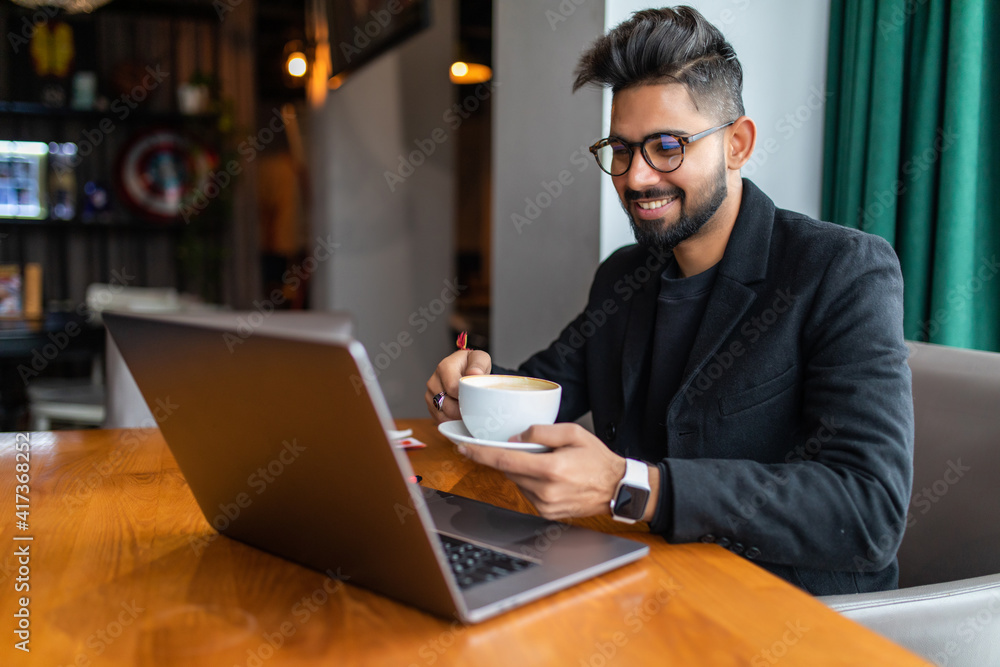 Indian young man smiling and working on laptop at cafe Indian young man smiling and working on laptop at cafe
