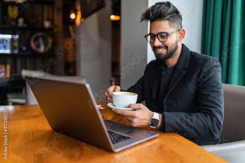 Indian young man smiling and working on laptop at cafe