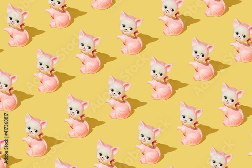 Creative pattern made with pastel pink cat or kitten vintage figurine on bright yellow background. Retro aesthetic idea. Romantic colorful concept.