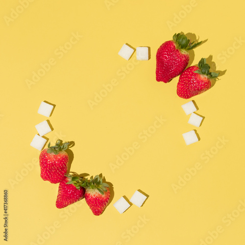 Creative frame made with strawberries and sugar cubes on bright yellow background. Flat lay food or fruit composition. Spring fruit idea.