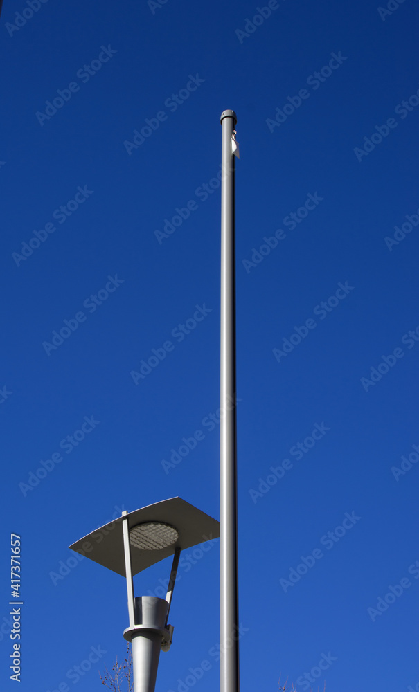one flagpole without flag and one lantern on a background of azure blue summer sky one flagpole without flag and one lantern on a background of azure blue summer sky