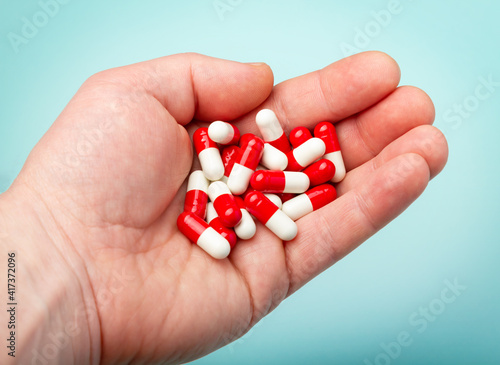 Close-up shot of red pill in hand over blue background.