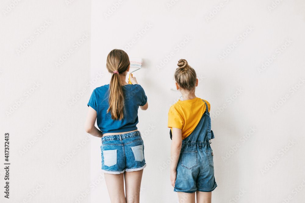 Obraz premium Two sisters are painting the walls of the house white, in denim overalls and a bright yellow T-shirt, home renovation