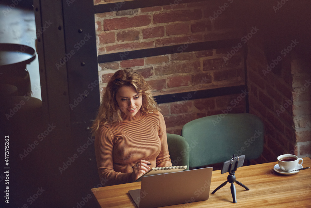 Obraz premium Woman taking notes while looking at computer screen