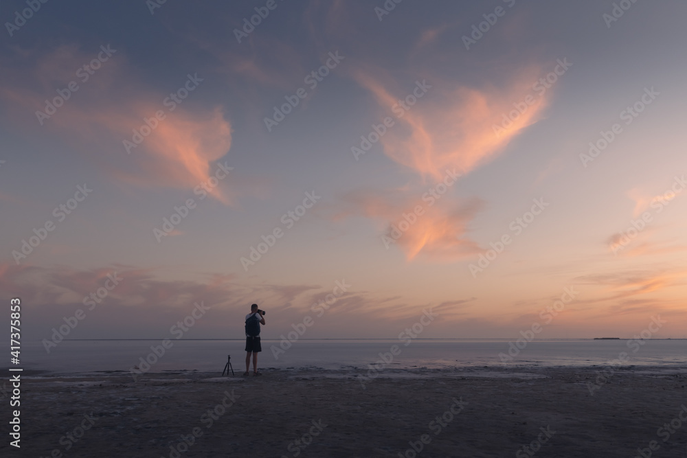 Photographer taking photo with tripod of ocean sunrise. Sunset on the sea with red glowing cloudy sky. Landscape photography
