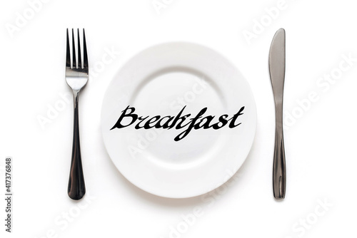 A white plate on which the word Breakfast is written standing on a tablecloth . The concept of a balanced diet, ration and medical fasting. Top view, white background, copy space.