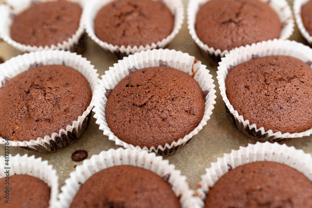 Brown chocolate muffins wrapped in white paper baked in the oven, lying on baking paper.. Brown chocolate muffins wrapped in white paper baked in the oven, lying on baking paper..