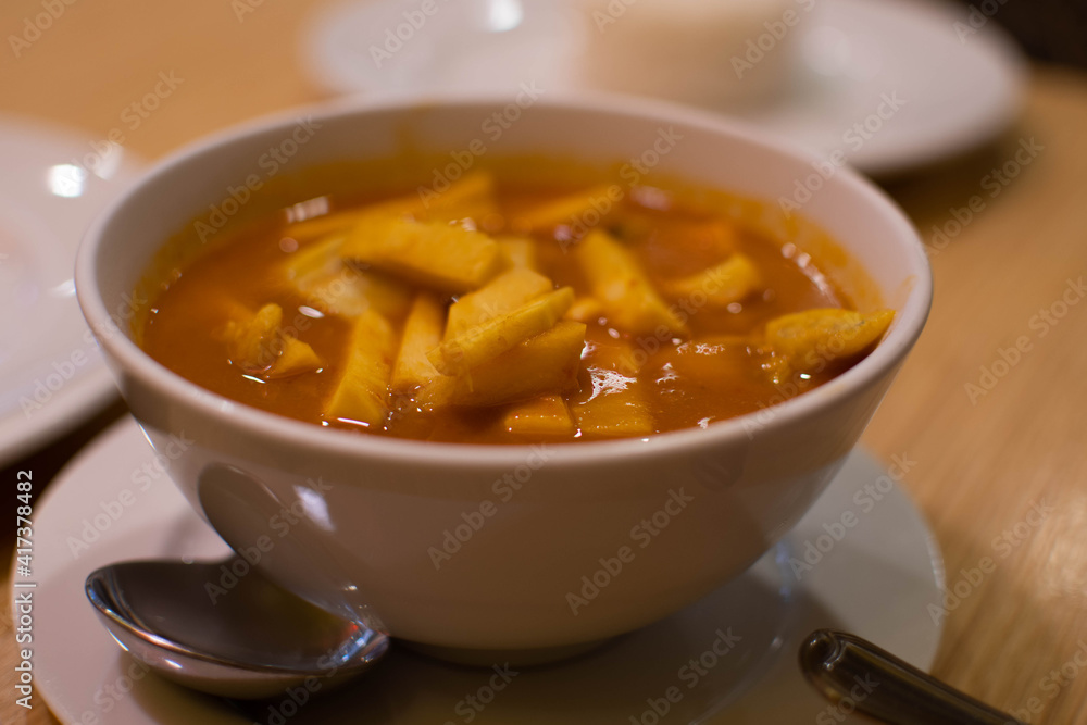 Slope view. Yellow curry, or sea fish sour curry with coconut shoots. The food of Thai people is popular to eat. A white cup of curry is placed on a wooden table in a local restaurant. Closeup. Slope view. Yellow curry, or sea fish sour curry with coconut shoots. The food of Thai people is popular to eat. A white cup of curry is placed on a wooden table in a local restaurant. Closeup.