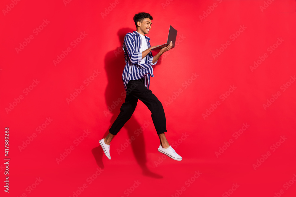 Obraz premium Full body profile side of young afro guy happy smile look browse internet laptop jump up isolated over red color background