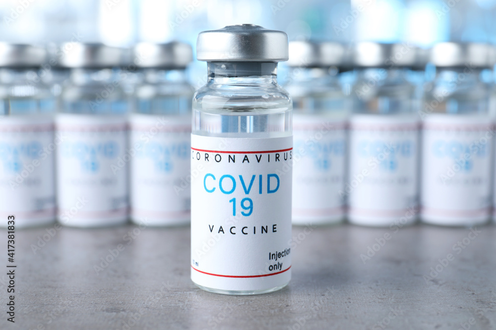 Glass vial with COVID-19 vaccine on grey table Glass vial with COVID-19 vaccine on grey table