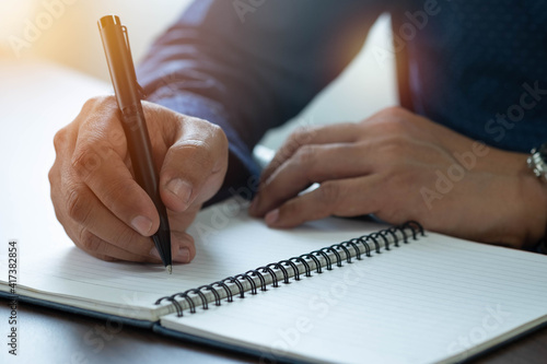 Close-up of man hand using writing pen memo on notebook paper or letter, diary on table desk office. Workplace for student, writer with copy space. business working and learning education concept. photo