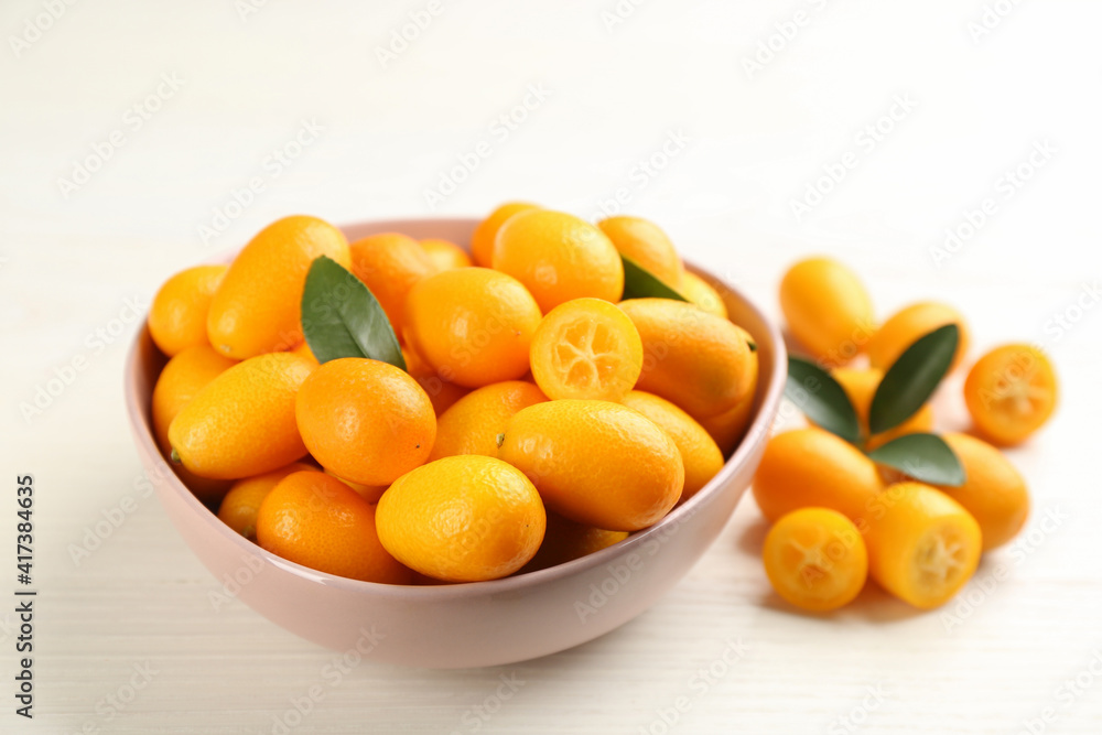 Fresh ripe kumquats with green leaves on white wooden table Fresh ripe kumquats with green leaves on white wooden table
