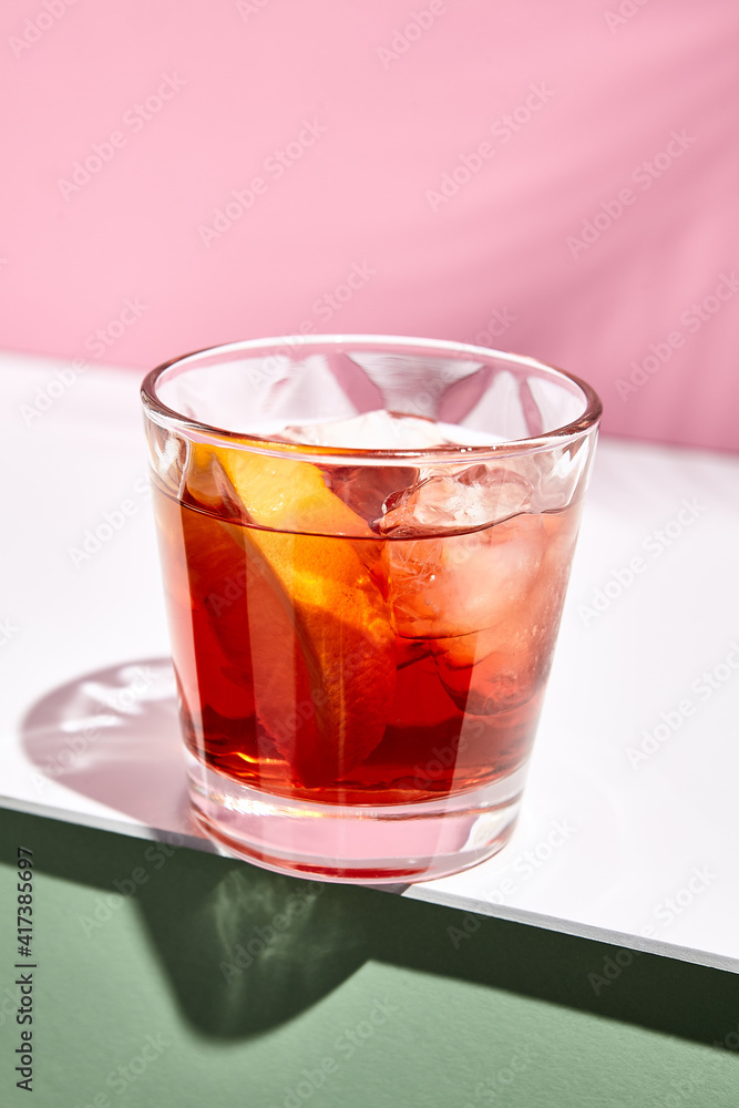 Negroni cocktail over pink background. Drink in rox glass in daylight with palm leaf hard shadow. Summer, tropical, fresh drink concept Negroni cocktail over pink background. Drink in rox glass in daylight with palm leaf hard shadow. Summer, tropical, fresh drink concept