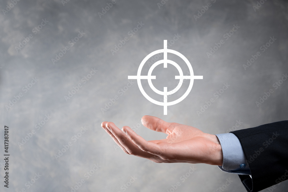 Targeting concept with businessman hand holding target icon dartboard sketch on chalkboard. Objective target and investment goal concept. Targeting concept with businessman hand holding target icon dartboard sketch on chalkboard. Objective target and investment goal concept.