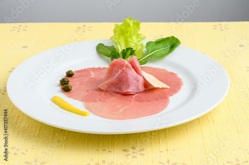 carpaccio on a white plate on a yellow tablecloth