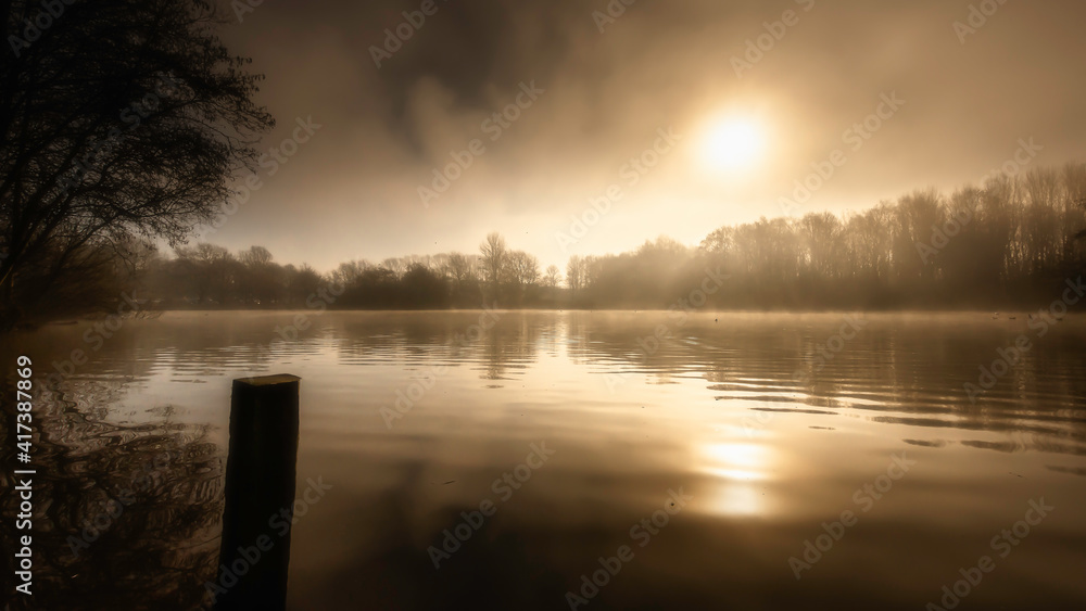 Sunrise over Westport lake in Stoke on Trent, Staffordshire, UK, on a foggy morning.Tranquil landscape scenery during golden hour.Beautiful and ethereal nature scene.