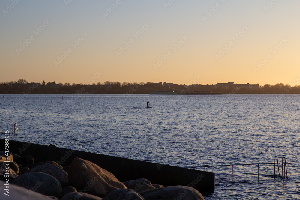 Man standing and dong paddle boarding on the sea outside Malmö Sweden during cold winter evening Man standing and dong paddle boarding on the sea outside Malmö Sweden during cold winter evening