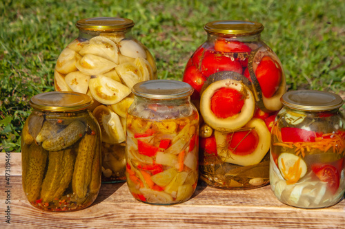 Homemade pickles in jars, rustic food and snacks stand on boards against a background of grass