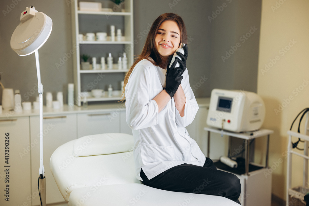 Consultation in cosmetology clinic. Female beauty doctor in white coat and black gloves shows her love to bottle of cream. Healthcare concept. Consultation in cosmetology clinic. Female beauty doctor in white coat and black gloves shows her love to bottle of cream. Healthcare concept.