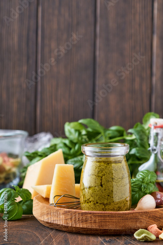 Jar with homemade pesto sauce on rustic background with parmesan cheese, olive oil, sause pesto, basil and garlic. Copy space background.
