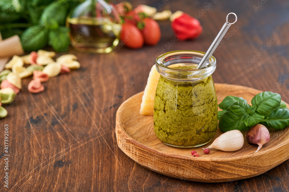 Jar with homemade pesto sauce on rustic background with parmesan cheese, olive oil, sause pesto, basil and garlic. Copy space background. Jar with homemade pesto sauce on rustic background with parmesan cheese, olive oil, sause pesto, basil and garlic. Copy space background.