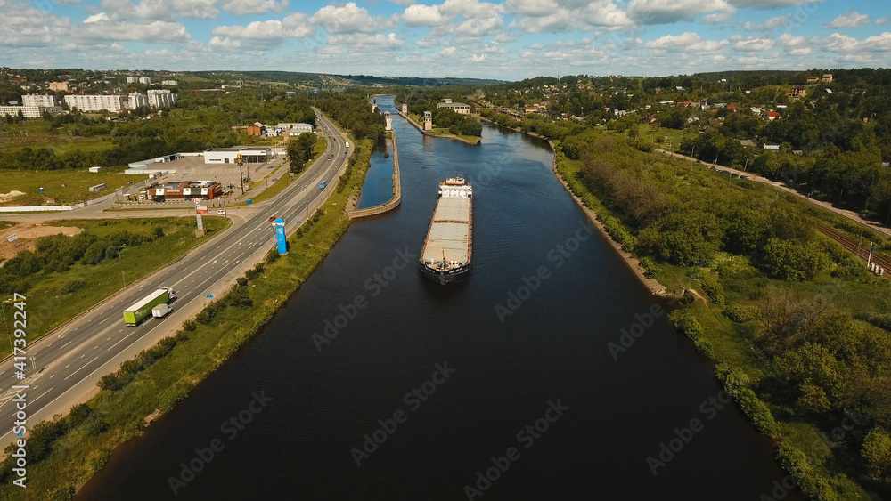Fototapeta premium Aerial view:Barge with cargo on the river. River, cargo barge, highway with cars.. Cargo ship on the river.