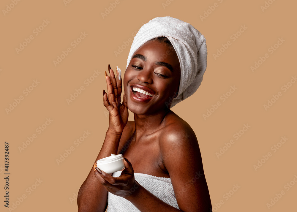 Beautiful young african american woman applying cream on face - obrazy, fototapety, plakaty 