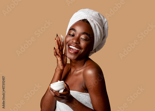 Beautiful young african american woman applying cream on face photo