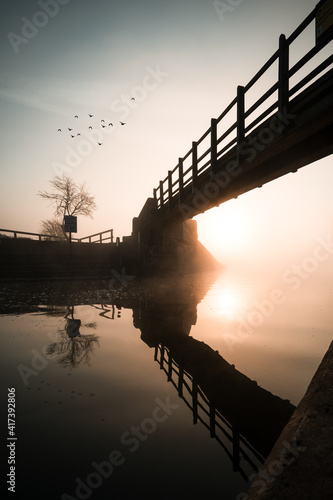 Sunrise from from under wooden foot bridge over river reflected in canal beautiful orange reflection crystal still tranquil water birds flying in sky reflected amazing sunset Trent Lock Nottingham