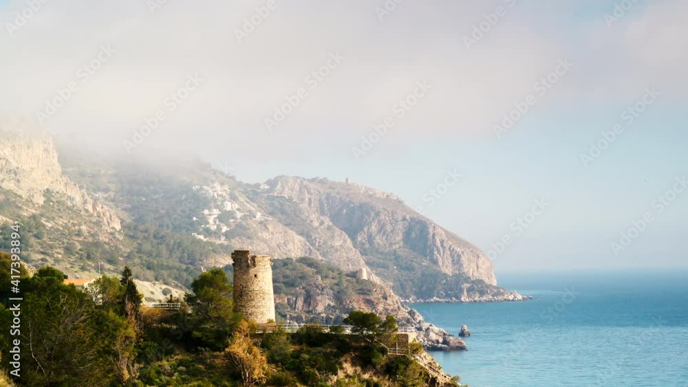 Time lapse of clouds moving over coastal landscape with watchtower. Torre Del Pino, tower on cliffs of Maro Cerro Gordo Natural Park, Malaga province, Costa Del Sol, Andalusia, Spain. Time lapse of clouds moving over coastal landscape with watchtower. Torre Del Pino, tower on cliffs of Maro Cerro Gordo Natural Park, Malaga province, Costa Del Sol, Andalusia, Spain.