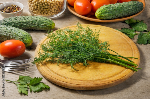 Fresh dill on a cutting board. Cucumbers, tomatoes and spices on a wooden table.