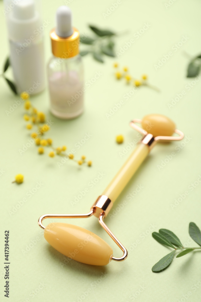 Natural face roller, cosmetic products and flowers on green background Natural face roller, cosmetic products and flowers on green background