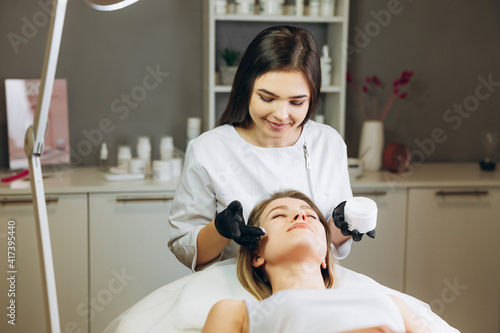 Fotografija Cosmetologist applying cream essence essential vitamins into face to improve client skin