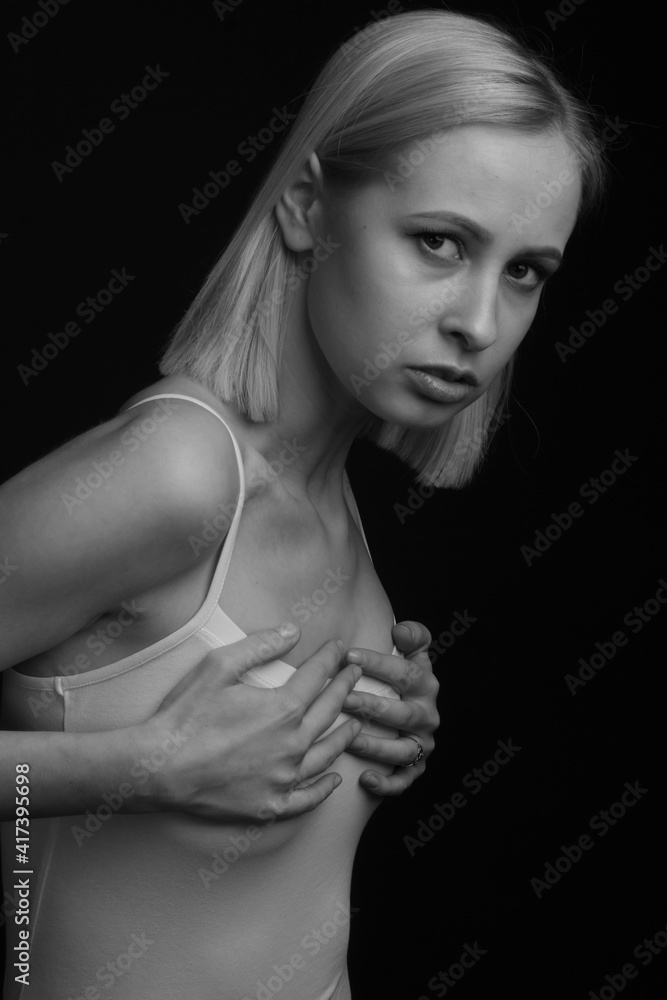 black and white portrait of a blonde on a black background. in a white tank top with straps. holding on to the chest black and white portrait of a blonde on a black background. in a white tank top with straps. holding on to the chest