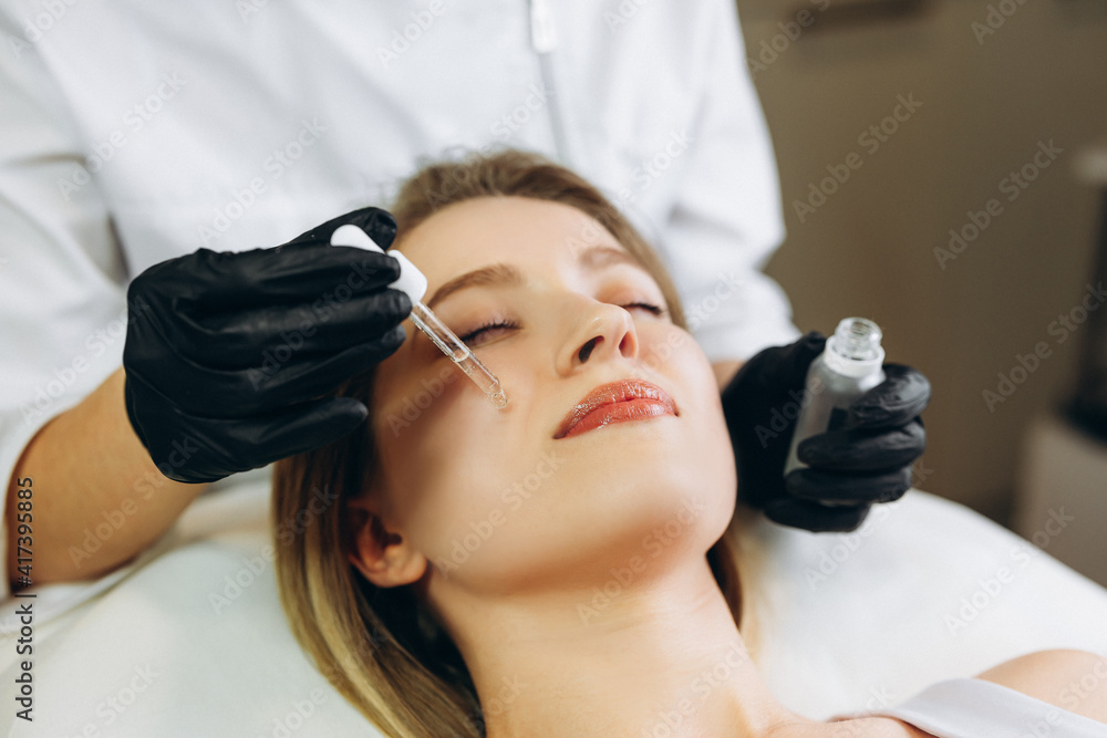 osmetologist applying serum essence essential vitamins oils water into face to improve client skin. Beauty expert makes beauty treatment for patient. Health, skin care, aethetic medicine concept osmetologist applying serum essence essential vitamins oils water into face to improve client skin. Beauty expert makes beauty treatment for patient. Health, skin care, aethetic medicine concept