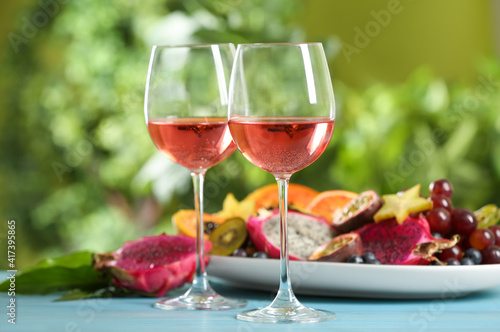 Delicious exotic fruits and wine on light blue wooden table