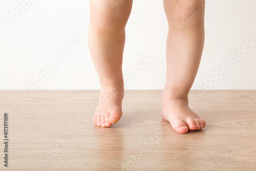 Baby girl barefoot on wooden floor background. Closeup. First steps. Front view.