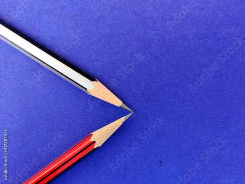 Copy space of red and black color pencil pointing each other on blue background