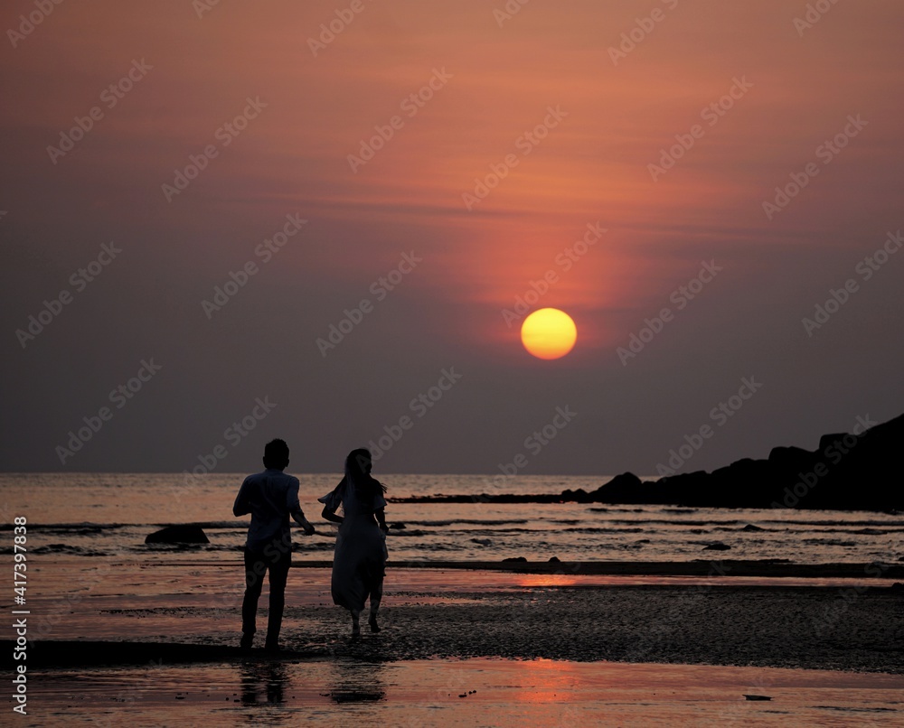 Beautiful sunset with silhouette asian couple at Layan Beach, Phuket, Thailand.