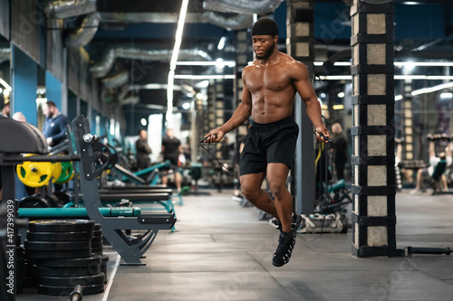 Shirtless muscular african man jumping with skipping rope in gym